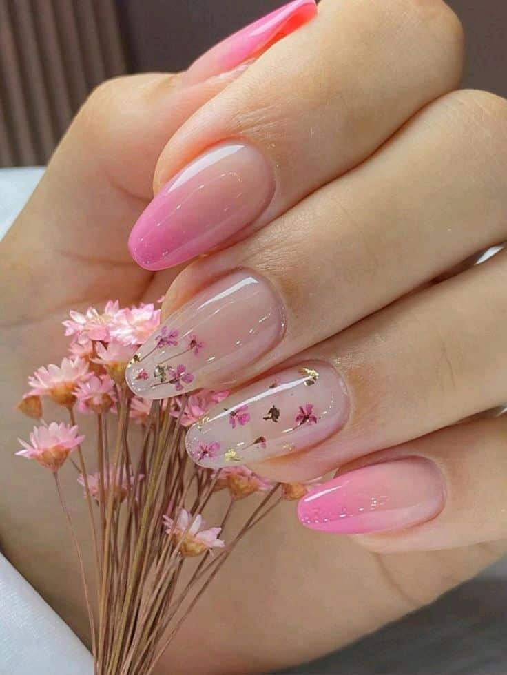 Unhas alongadas em gel com acabamento rosa e decoração floral delicada, segurando flores secas.