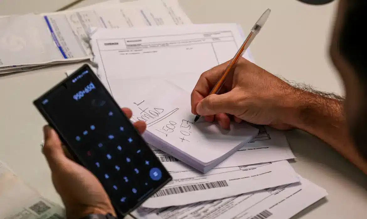 "Pessoa calculando dívidas com uma calculadora e anotações, cercada por documentos financeiros."