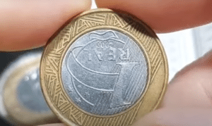 Moeda de 1 real com erro de reverso invertido, mostrando a parte de trás da moeda estampada incorretamente.