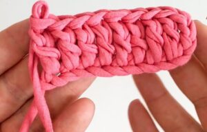 Ponto alto em crochê, feito com fio de camiseta rosa, mostrando a textura do trabalho manual