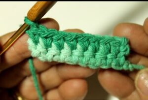 Ponto baixo em crochê com fio em degradê verde, mostrando a técnica detalhada com agulha.