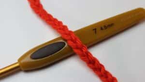 Ponto corrente em crochê com fio vermelho e agulha 4.5mm, mostrando a técnica de início de trabalho.