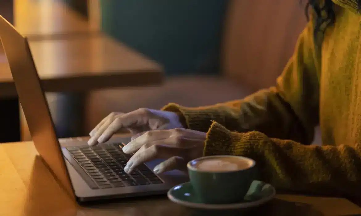 "Pessoa usando um laptop para acessar um site, com uma xícara de café ao lado."