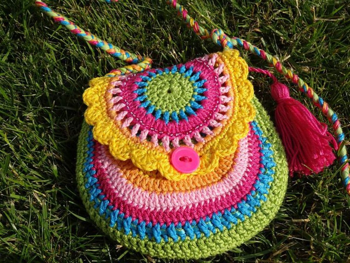Bolsinha colorida de crochê com detalhes em pink, amarelo e verde, com botão e tassel.
