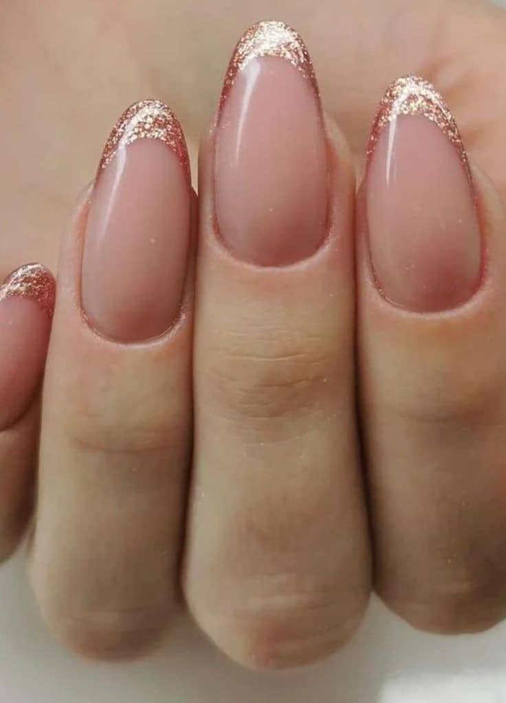 Unhas decoradas com francesinha moderna em glitter dourado sobre base nude.