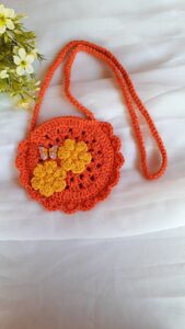 Linda bolsinha de crochê laranja com flores amarelas decorativas e detalhe de borboleta, ideal para crianças e netinhas.