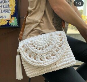 Clutch de crochê branca com textura artesanal e alça de couro marrom.