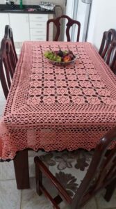 Toalha de crochê artesanal rosa sobre mesa de jantar com fruteira no centro, em cozinha residencial