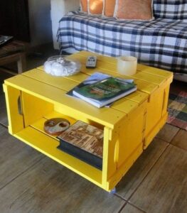 Mesa de centro feita com caixas de madeira recicladas pintadas de amarelo, decorada com livros e objetos.