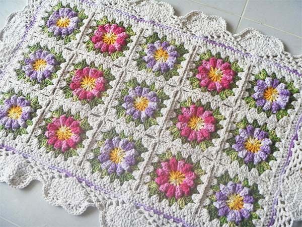 Tapete de crochê floral com quadrados coloridos em tons de branco, rosa, lilás, amarelo e verde, com bordas delicadas.