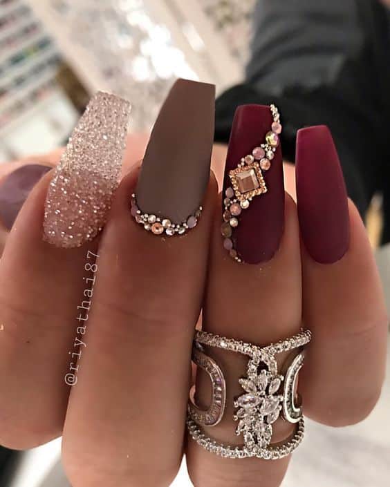 Unhas em gel personalizadas com glitter, pedrarias e acabamento fosco em tons de vinho e nude, tendência para mulheres acima de 50 anos