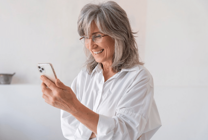 Mulher com cabelo grisalho sorrindo enquanto usa o celular.