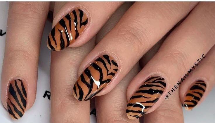 Unhas com estampa de tigre em tons de laranja e preto.