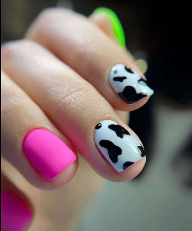Unhas coloridas com estampa de vaca em fundo branco e detalhes em rosa neon.