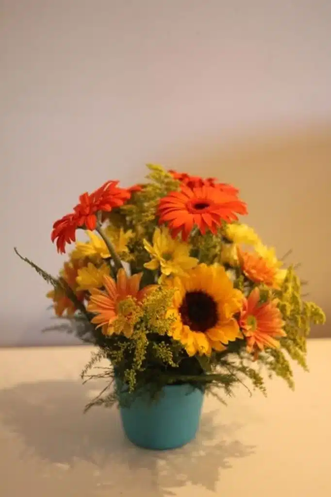 Arranjo colorido de flores do campo em vaso azul, com girassóis e flores laranjas