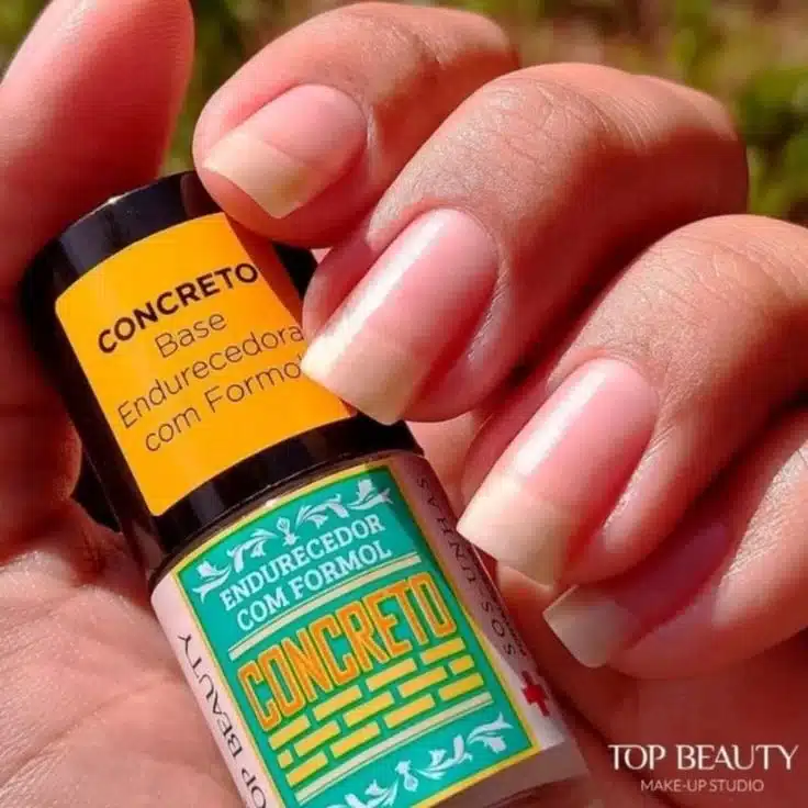 Imagem de base endurecedora com formol Top Beauty Concreto sendo aplicada em unhas naturais, destacando sua fórmula fortalecedora