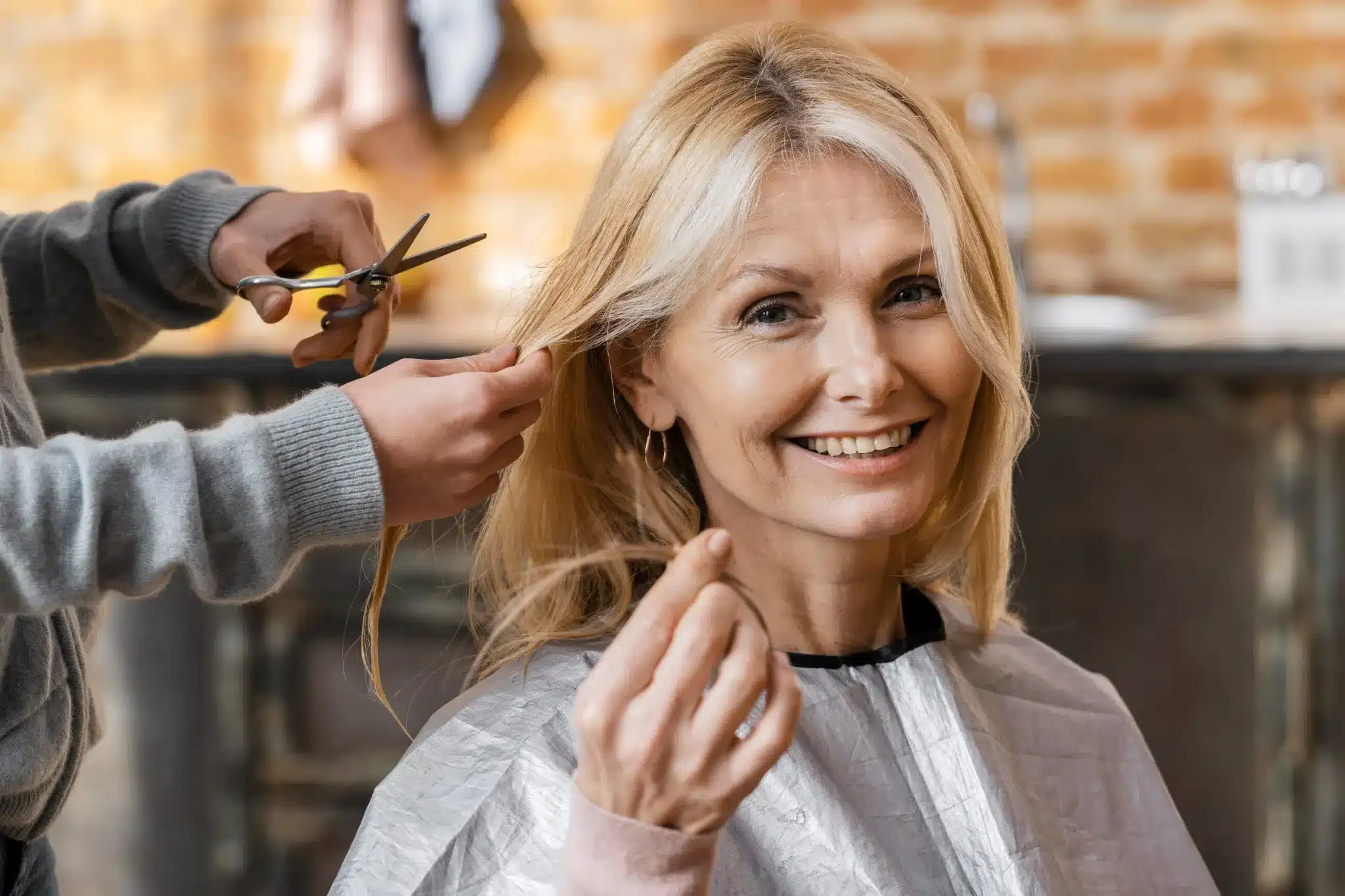 Mulher madura sorrindo enquanto recebe um corte de cabelo moderno em salão, valorizando a beleza natural aos 70 anos.