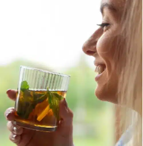 Mulher sorrindo enquanto segura um copo de chá de ervas