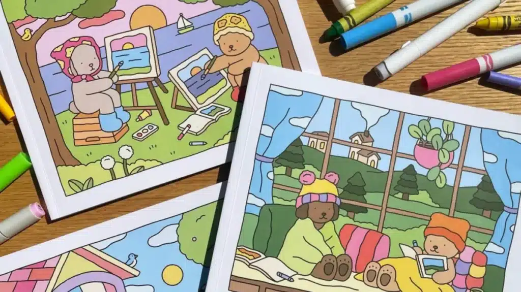 Livros de colorir Bobbie Goods com ilustrações de ursinhos em ambientes ao ar livre e internos, com marcadores coloridos ao redor.