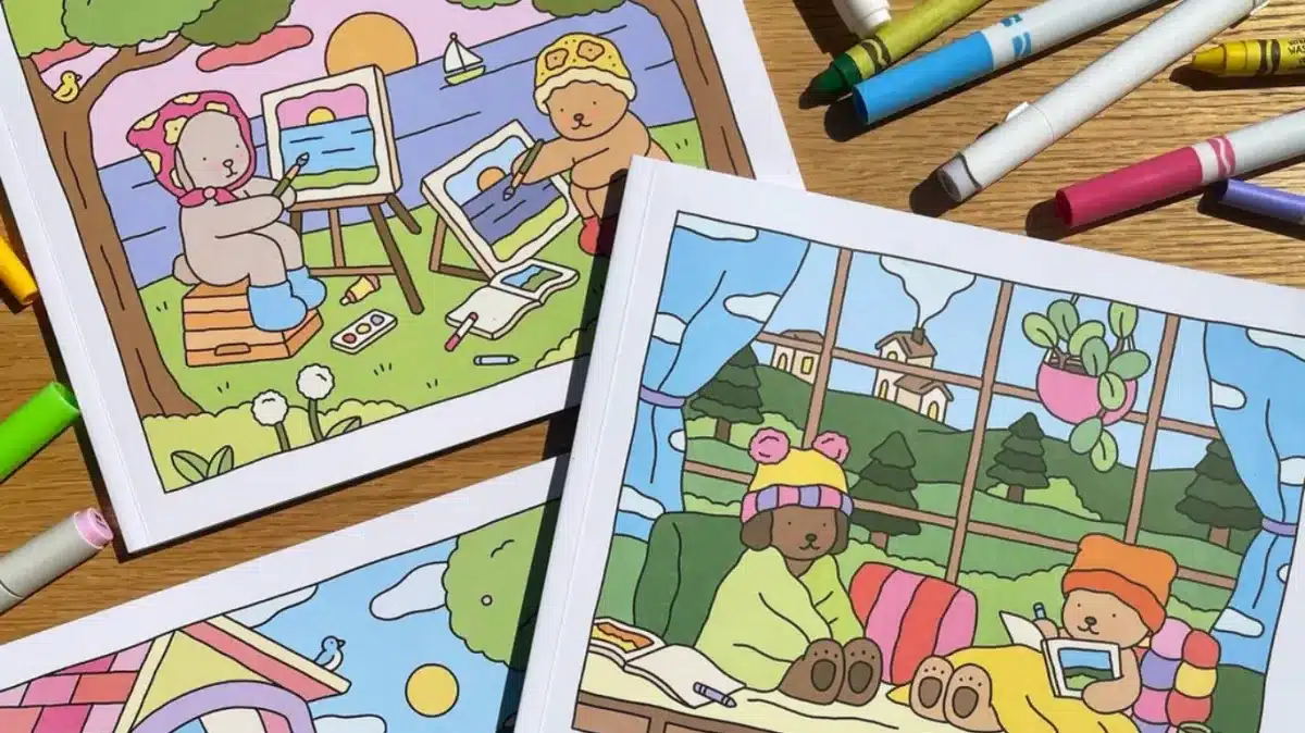 Livros de colorir Bobbie Goods com ilustrações de ursinhos em ambientes ao ar livre e internos, com marcadores coloridos ao redor.