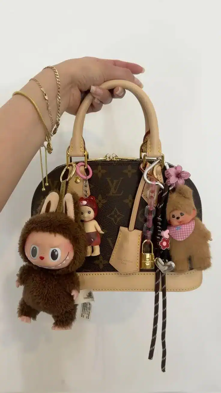 Bolsa Louis Vuitton com chaveiros fofos de bonecos peludos e acessórios coloridos pendurados.