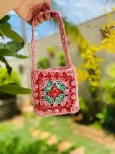 Bolsinha infantil de crochê em formato square com cores rosa, vermelho e verde.