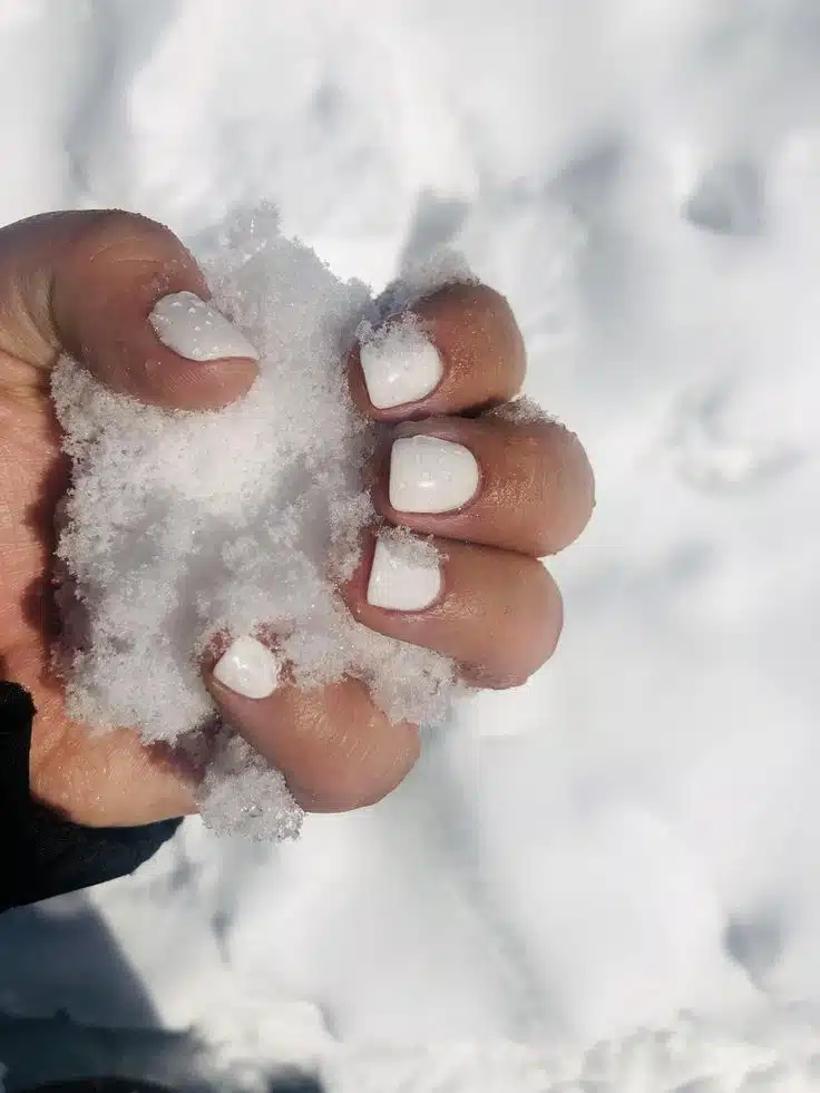 Unhas curtas pintadas com esmalte branco neve em ambiente com neve
