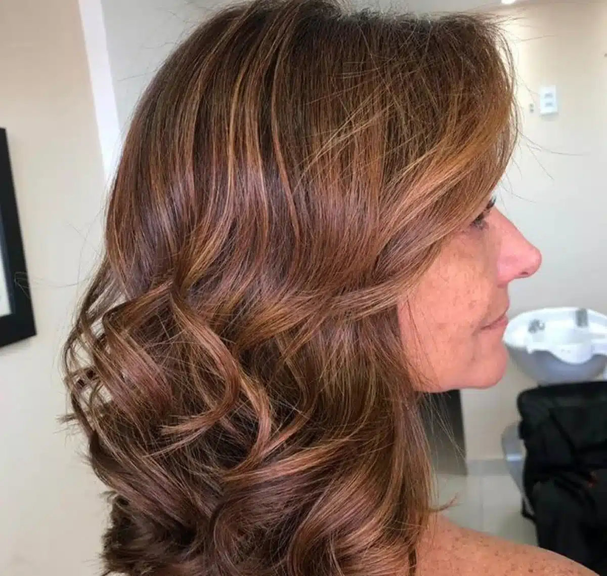 Cabelos iluminados em mulher madura com tons naturais de mel, caramelo e amêndoa, realçando a beleza aos 50+.