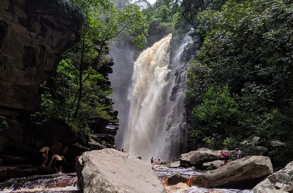 Cachoeira imponente na Bahia cercada por vegetação densa e pedras, com visitantes apreciando a natureza.