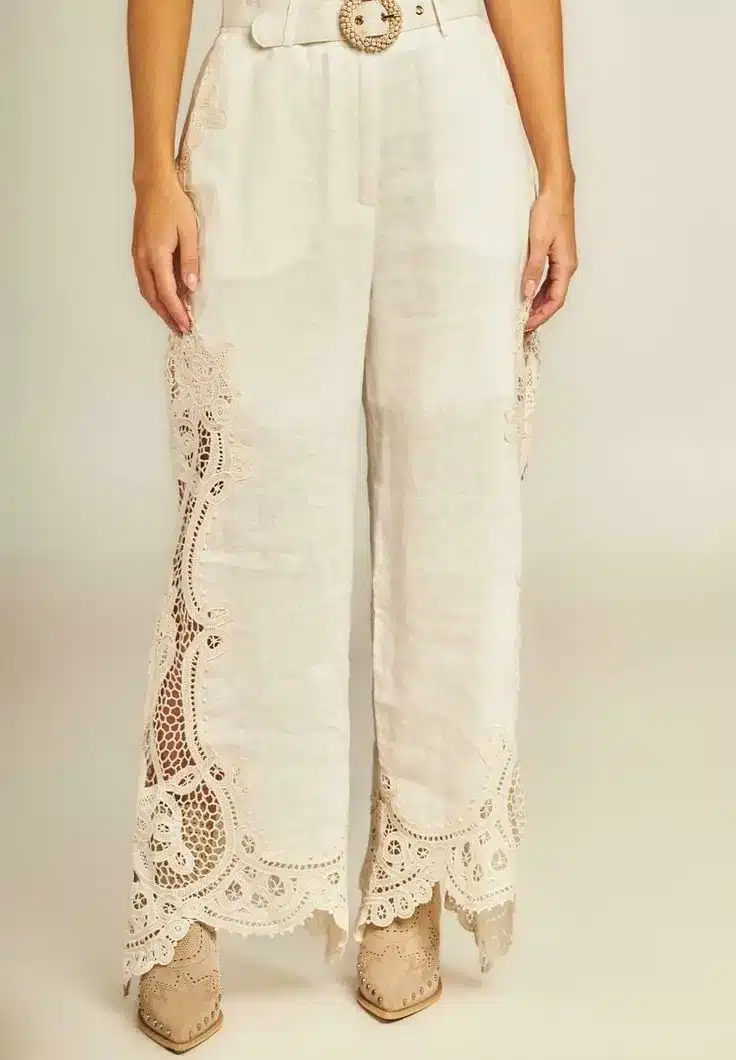 Calça de alfaiataria off-white com aplicações em crochê nas laterais e barra.
