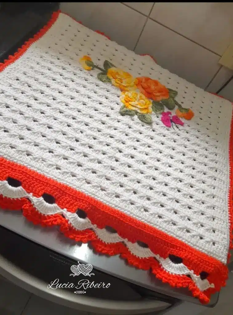 Capa de crochê branca com borda laranja e flores decorativas para proteção de fogão.