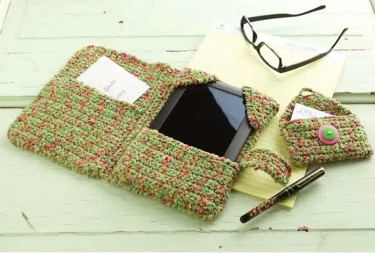 Capinha de crochê colorida feita à mão, mostrando bolso para cartão e botão decorativo, com tablet dentro.