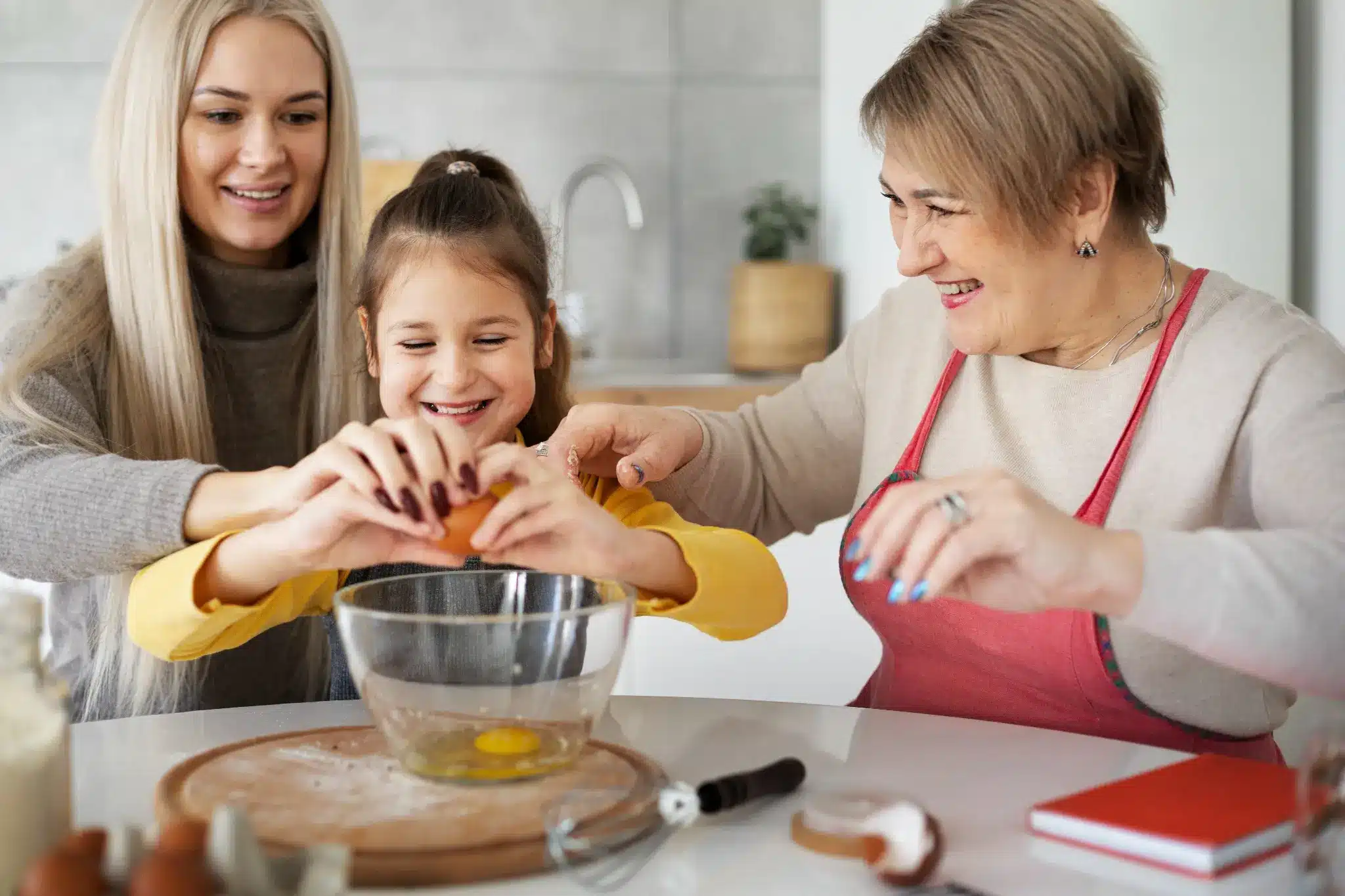 Criança, mãe e avó preparando uma receita juntas na cozinha, representando um momento especial para o Dia das Mães.