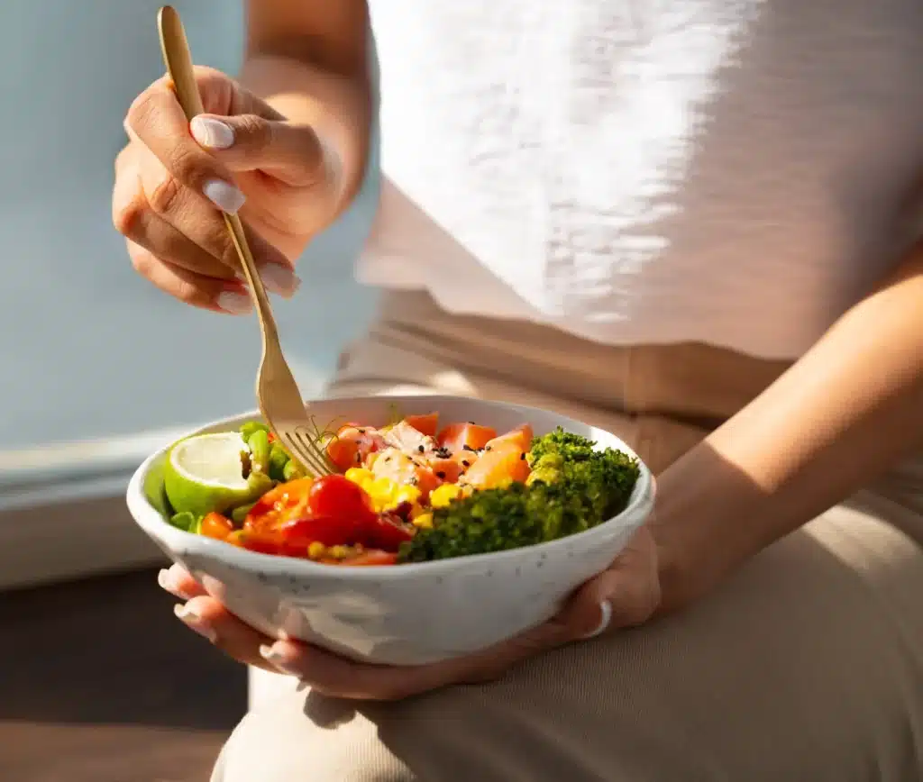 Mulher segurando uma tigela com salmão, legumes e verduras, representando uma alimentação saudável para fortalecer as unhas.