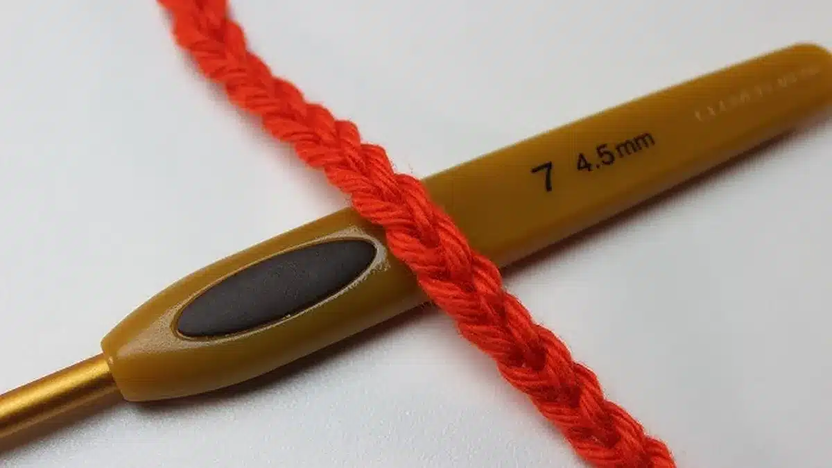 Agulha de crochê número 7 com fio vermelho, mostrando o ponto corrente, a base do crochê