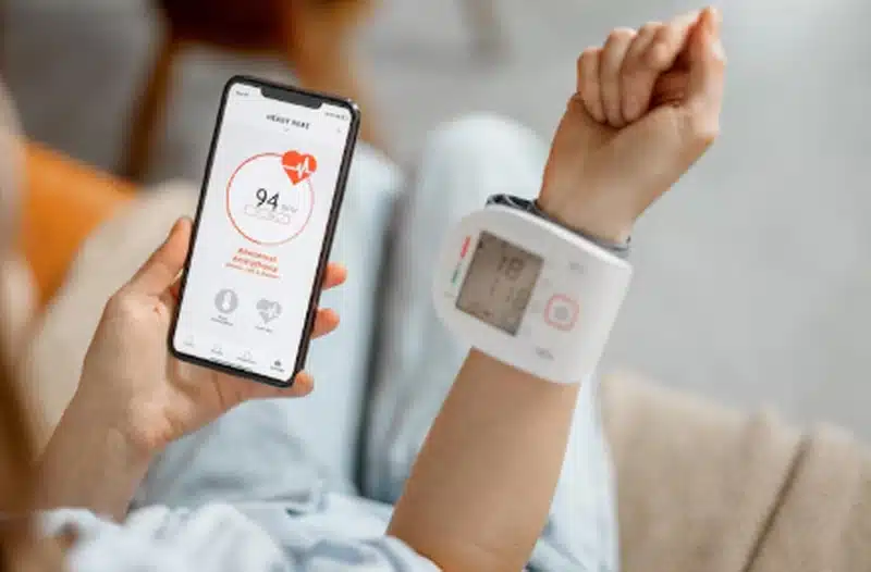 Pessoa usando aplicativo de saúde no celular e monitor digital no pulso para acompanhar pressão arterial e frequência cardíaca.