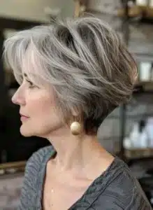 Mulher com corte pixie moderno e prático, mostrando laterais curtas e franja longa em cabelo grisalho estilizado.