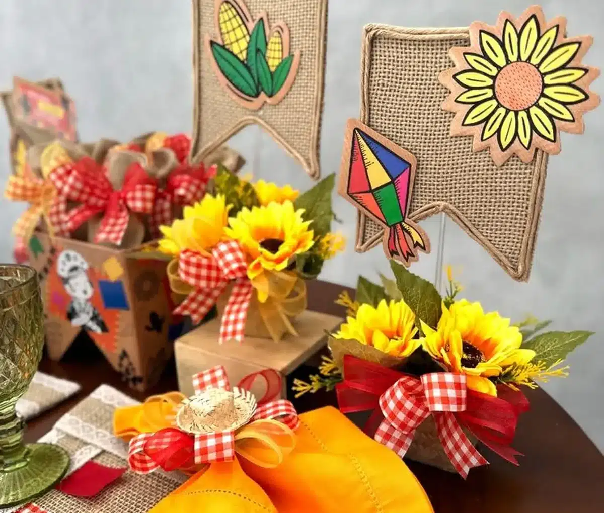 Decoração de mesa para festa de São João com arranjos de girassóis, bandeirinhas de juta, e detalhes em fita xadrez vermelho