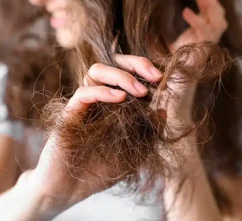 Cabelo ressecado e com frizz sendo segurado por uma mulher, mostrando falta de hidratação nos fios.