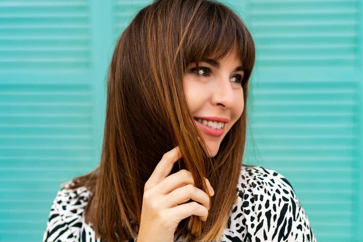 Mulher sorrindo com cabelo castanho médio, liso e franja reta estilizada