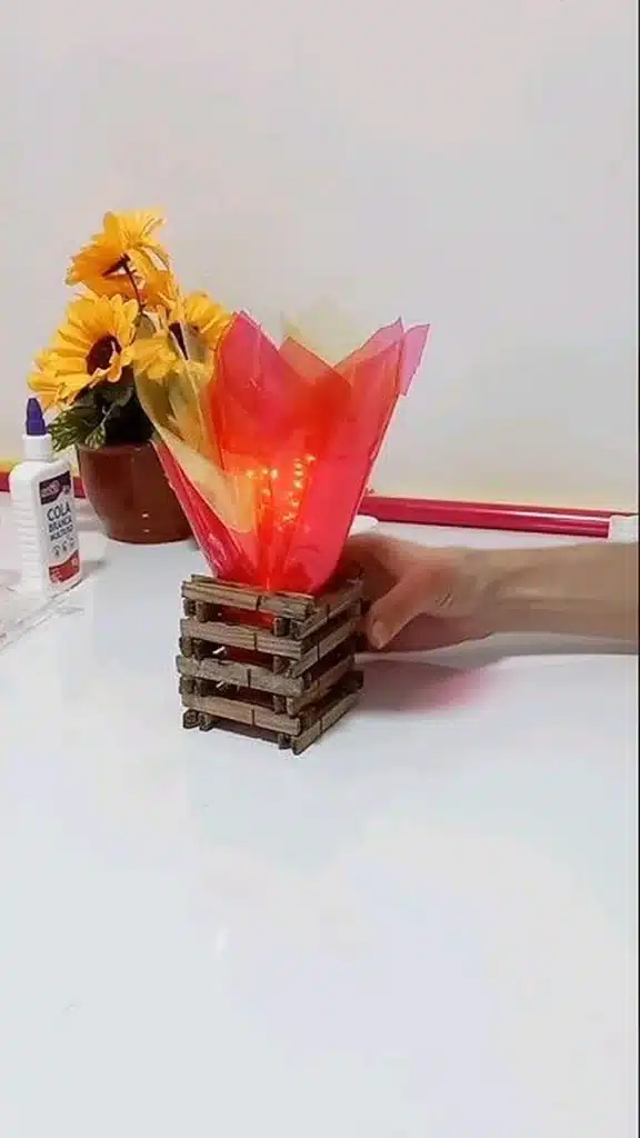 Mini fogueira decorativa com luminária de luz amarela feita com palitos de madeira e papel celofane colorido