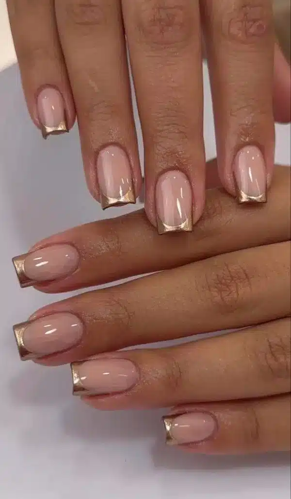 Unhas quadradas com francesinha metálica dourada sobre base nude, tendência para o inverno de 2025.