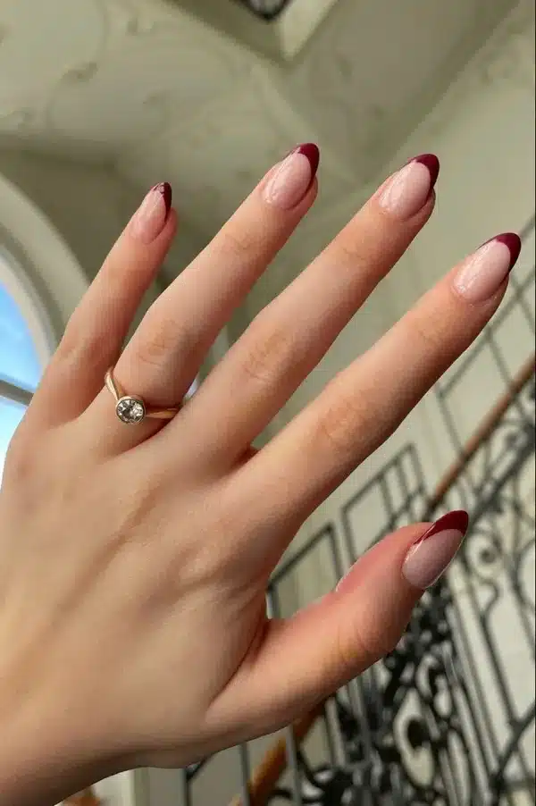 Unhas no formato amendoado com francesinha vinho sobre base nude, tendência para o inverno de 2025.