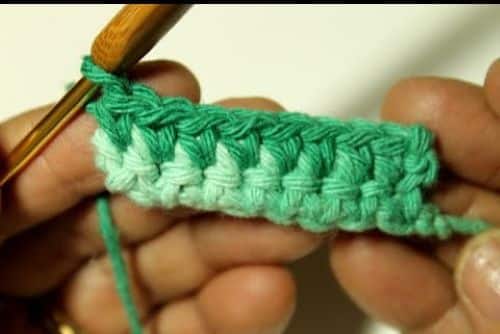 Execução do ponto baixo no crochê com fio verde e agulha de madeira
