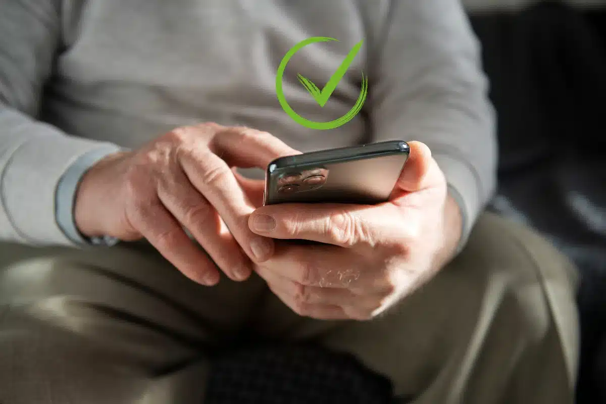 Pessoa idosa usando smartphone com símbolo de confirmação verde sobreposto.