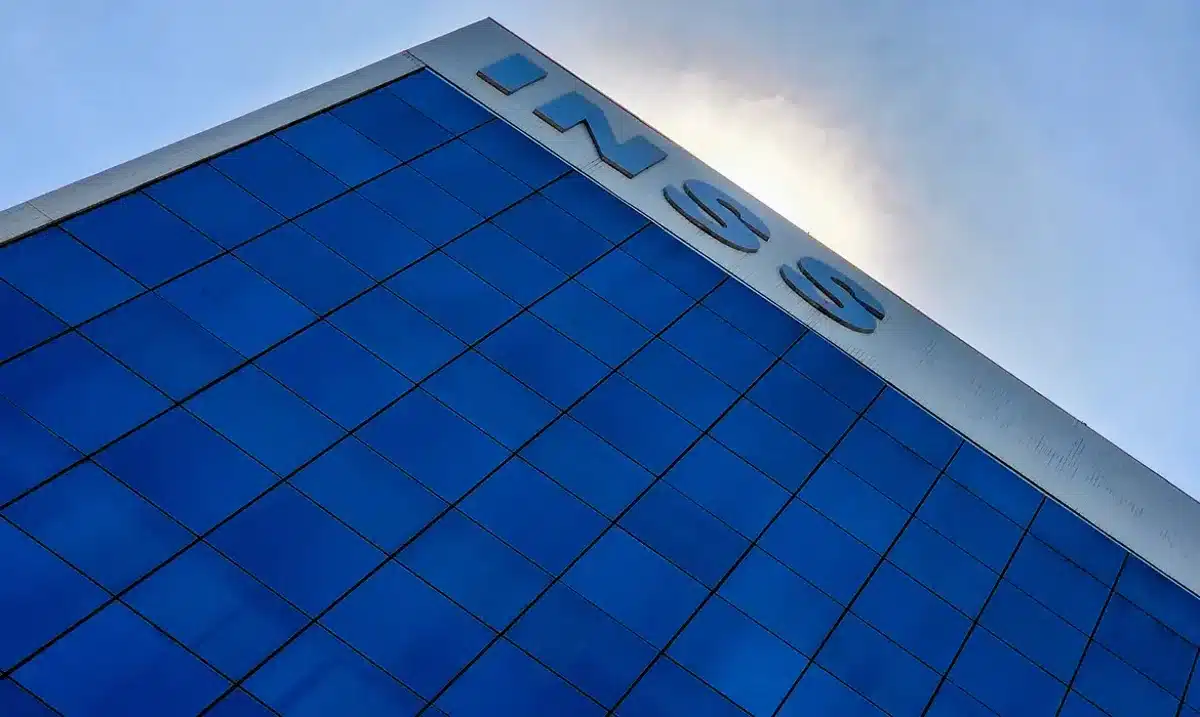 Prédio do INSS com fachada azul refletindo o céu.