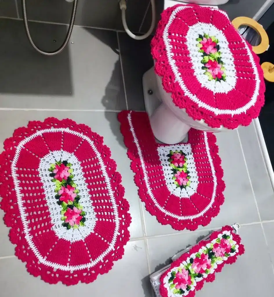 Jogo de banheiro em crochê artesanal com flores rosas, branco e verde, com peças para tampa do vaso, tapetes e capa para papel higiênico.