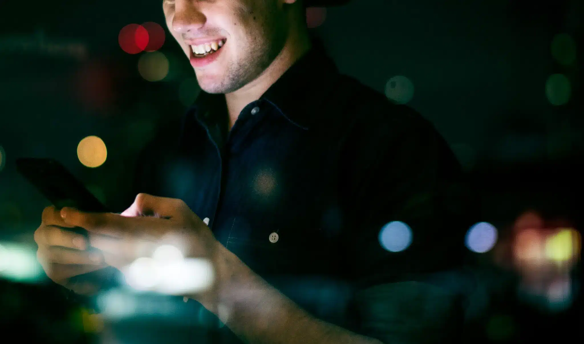 Jovem adulto sorrindo enquanto usa smartphone à noite em ambiente urbano