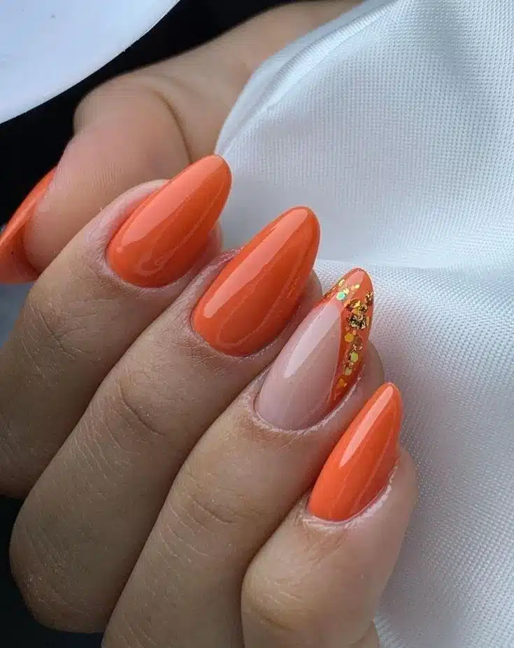 Unhas com esmalte laranja vibrante e detalhe decorativo com brilho dourado