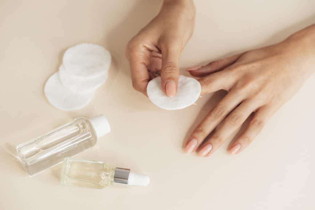 Mãos com unhas cuidadas usando algodão e produtos de manicure
